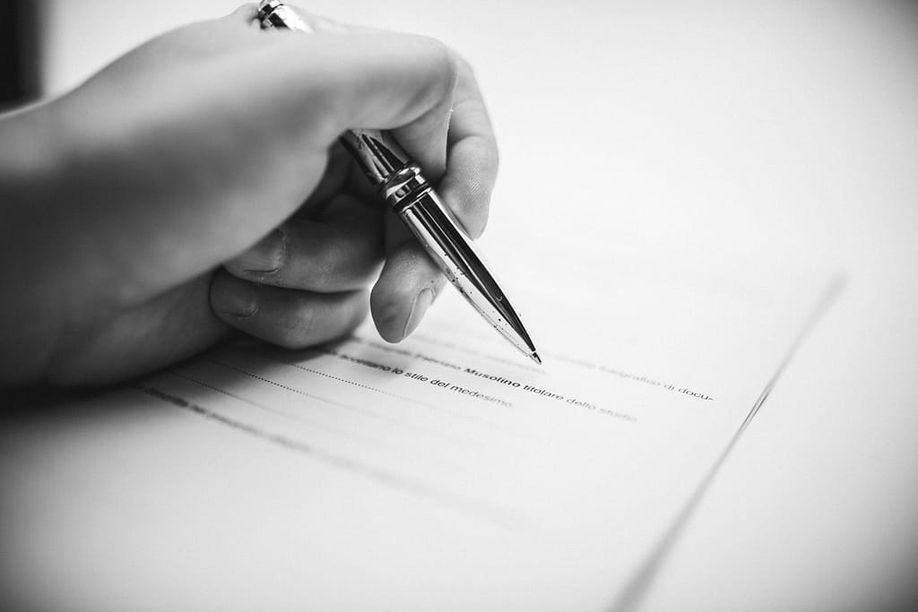 La firma del contratto per il servizio fotografico Dettaglio della mano del fotografo con una penna su un contratto di matrimonio, che simboleggia l'accordo e la trasparenza nel processo di scelta del professionista giusto.