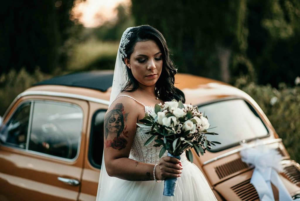 Pacchetto Matrimonio La Tua Storia La sposa con il bouquet in mano e la fiat cinquecento decorata.