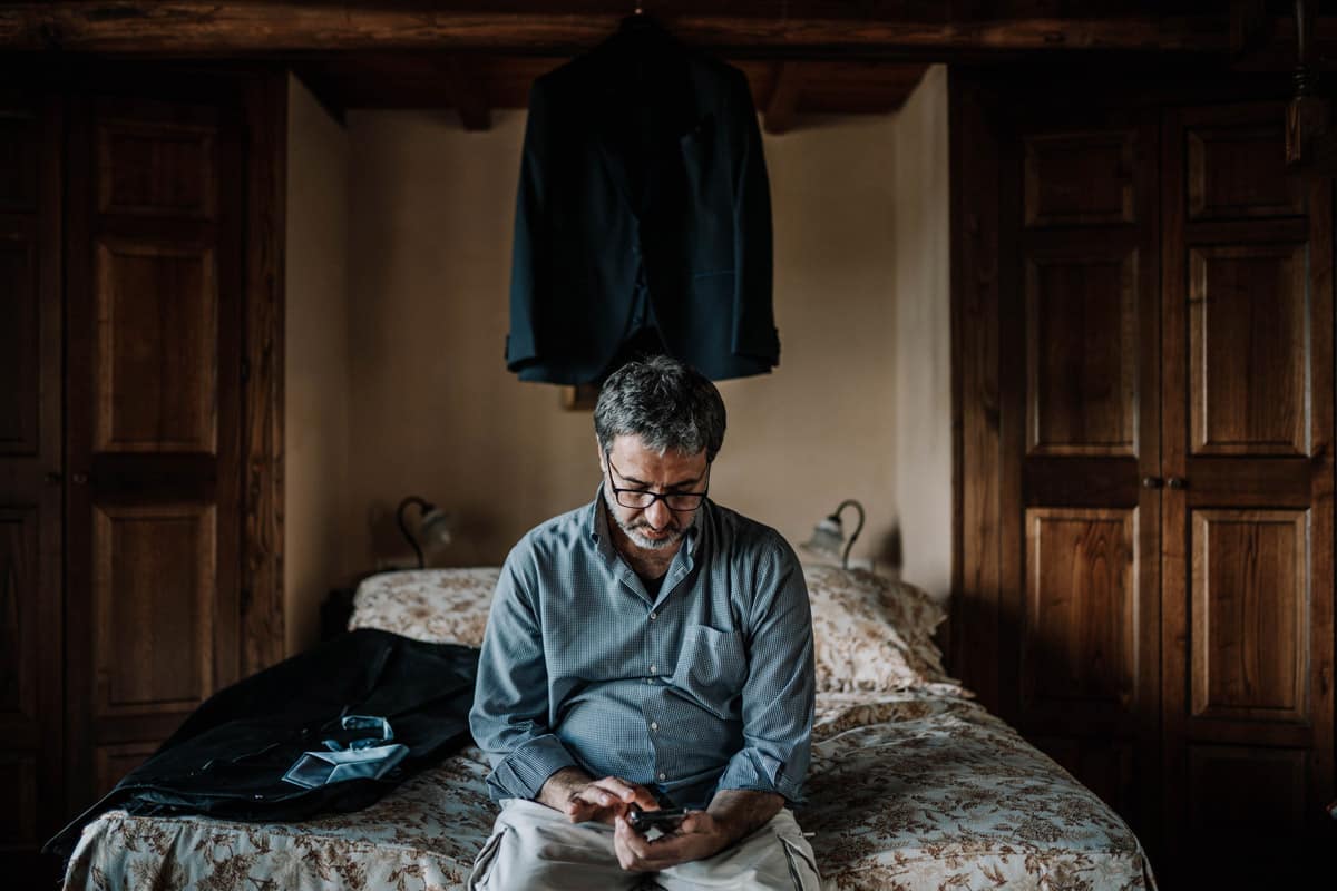 Momento di Riflessività: Lo Sposo e il Suo Messaggio Sposo sul letto che legge un messaggio sul cellulare durante la preparazione