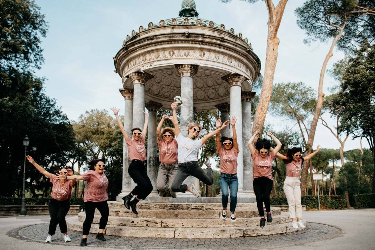 Futura sposa che salta con il bouquet insieme alle sue amiche a Villa Borghese.