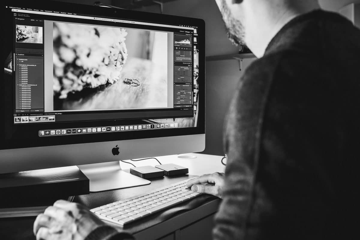 Dettaglio di Fabrizio Musolino impegnato nell'editing di una foto di fedi nuziali su monitor Mac. Si vedono le mani in fase di post-produzione professionale e parte del volto, a testimonianza del flusso di lavoro rapido del Metodo Zero Problemi.