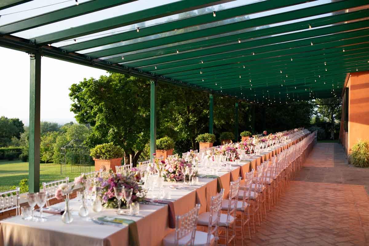 Allestimento elegante con composizioni floreali su tavolo lungo in terrazza con vista