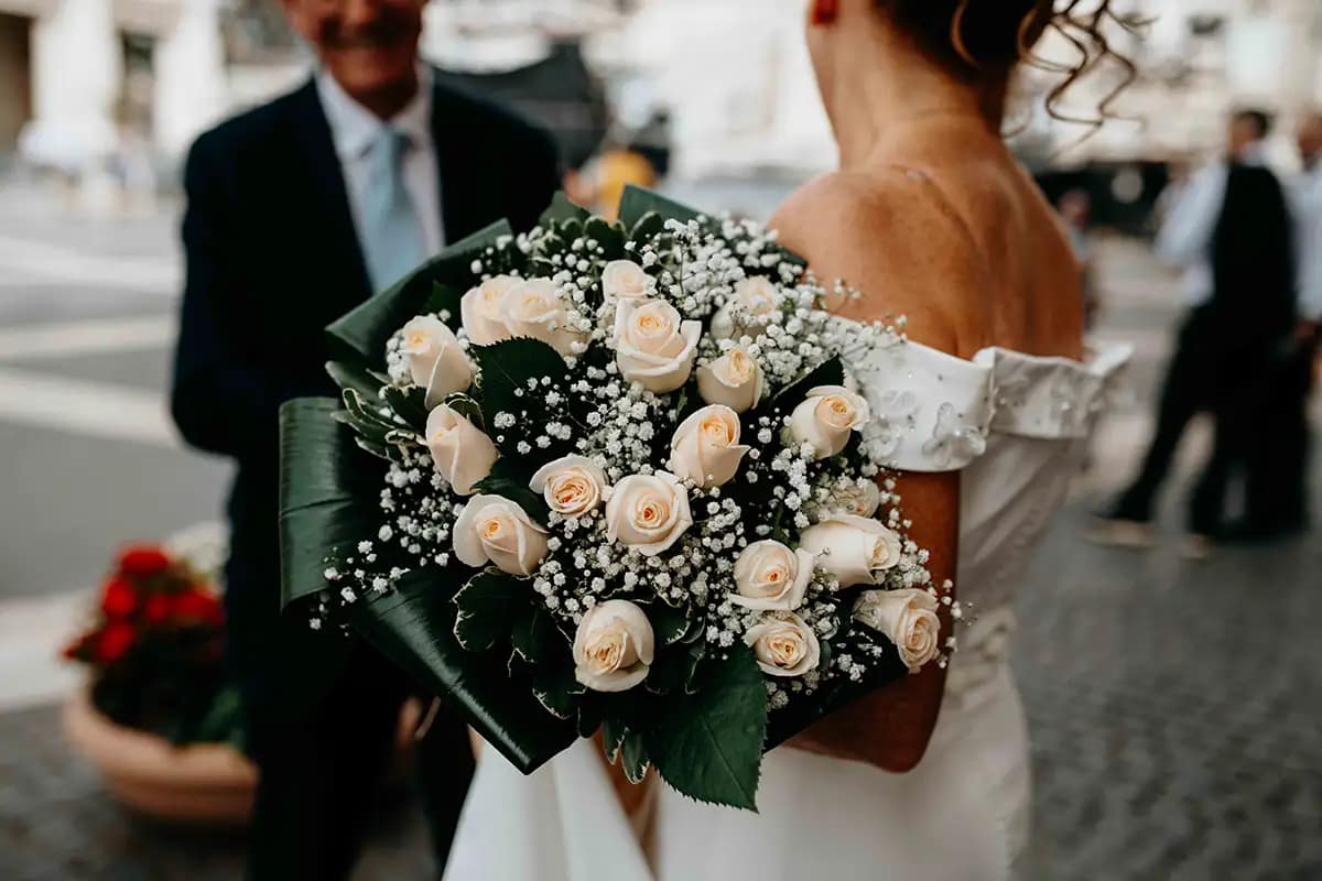 Dettaglio del bouquet della sposa appoggiato su un elemento storico in Piazza del Campidoglio, Roma. Atmosfera pre-cerimonia civile.