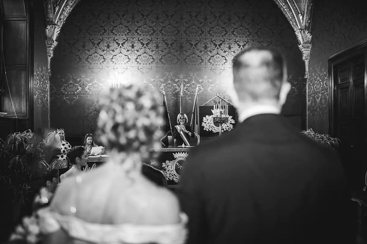 cerimonia-matrimonio-sala-rossa-campidoglio-roma Momento dell'applauso durante la cerimonia civile in Sala Rossa al Campidoglio. Sposi visti di schiena e celebrante sorridente. Fotografia di matrimonio emozionale a Roma.