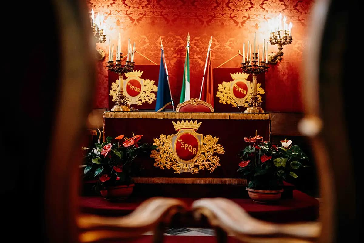 sala-rossa-campidoglio-interno-cerimonia-civile Interno della Sala Rossa del Campidoglio a Roma: sedie in velluto rosso, stemma del Comune e bandiere (Italia, Europa, Roma). Luogo esclusivo per matrimoni civili