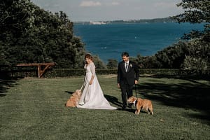 Laura e Luigi posano con i loro due cani con lo sfondo del lago di Bracciano nel giardino della Tenuta San Liberato.