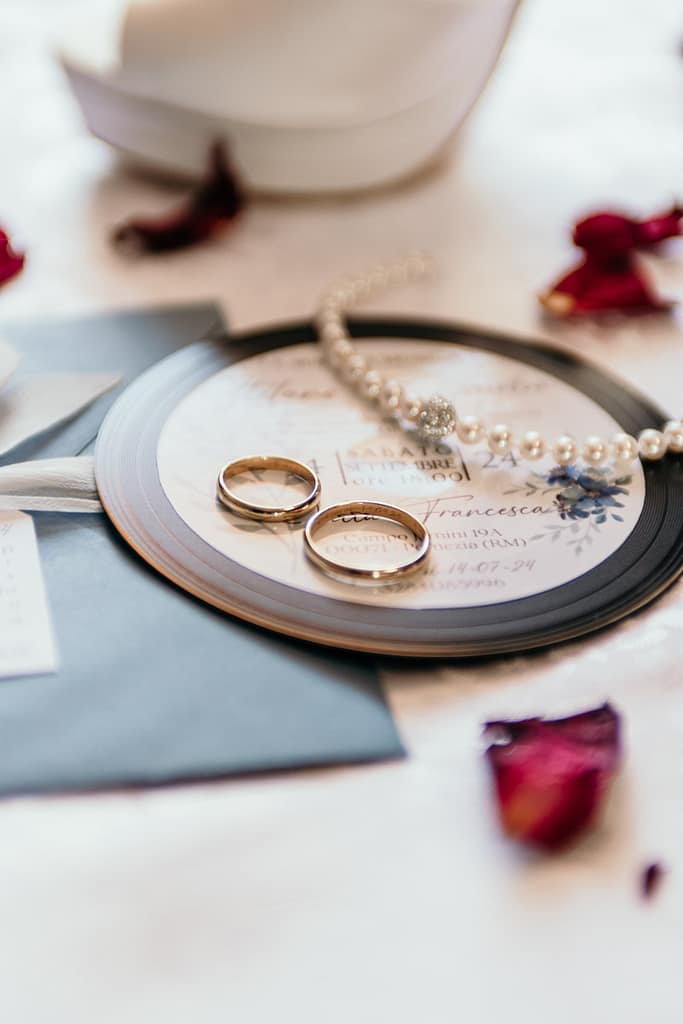 Dettagli della preparazione: collana, partecipazione, fedi nuziali e petali di fiori. Dettagli della preparazione del matrimonio con collana, fedi nuziali, partecipazione e petali di fiori.